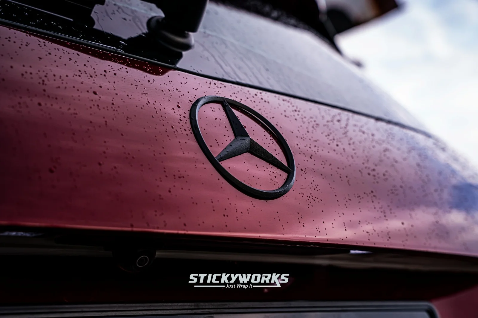 StickyWorks Mercedes badge close-up with water beads on gloss red wrap showcasing smooth surface and protection