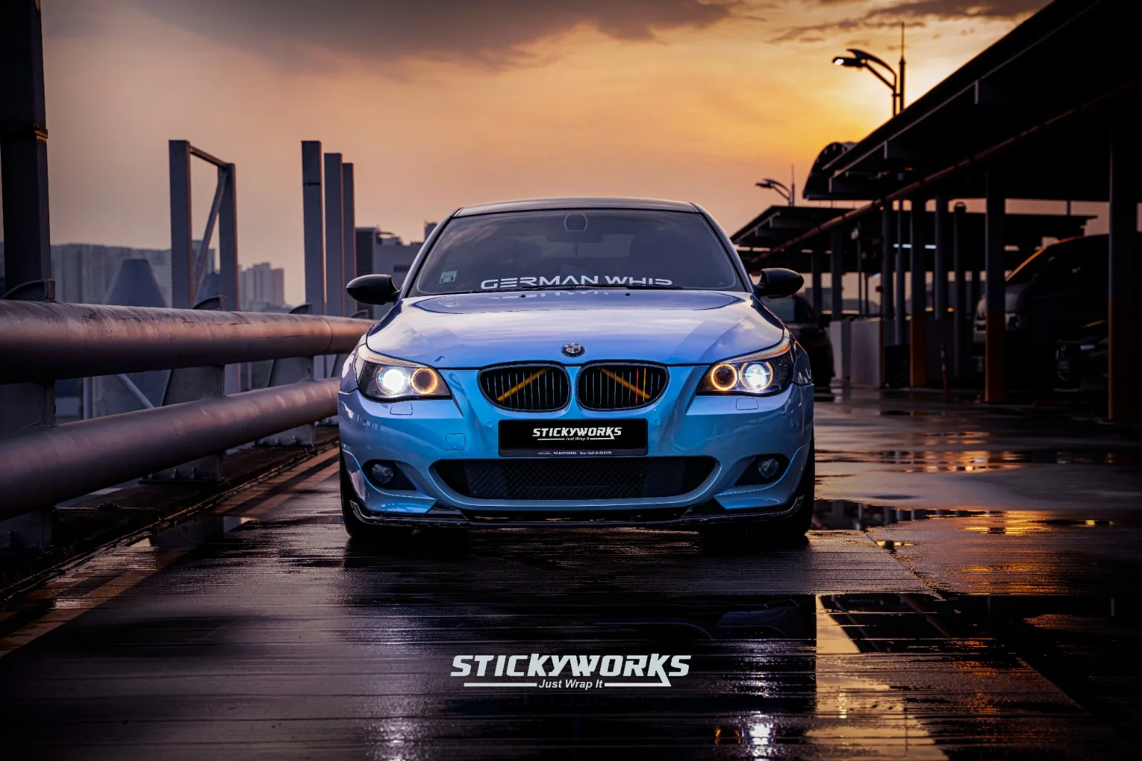 Blue BMW M5 reflected on wet surface highlighting high-gloss vinyl wrap finish