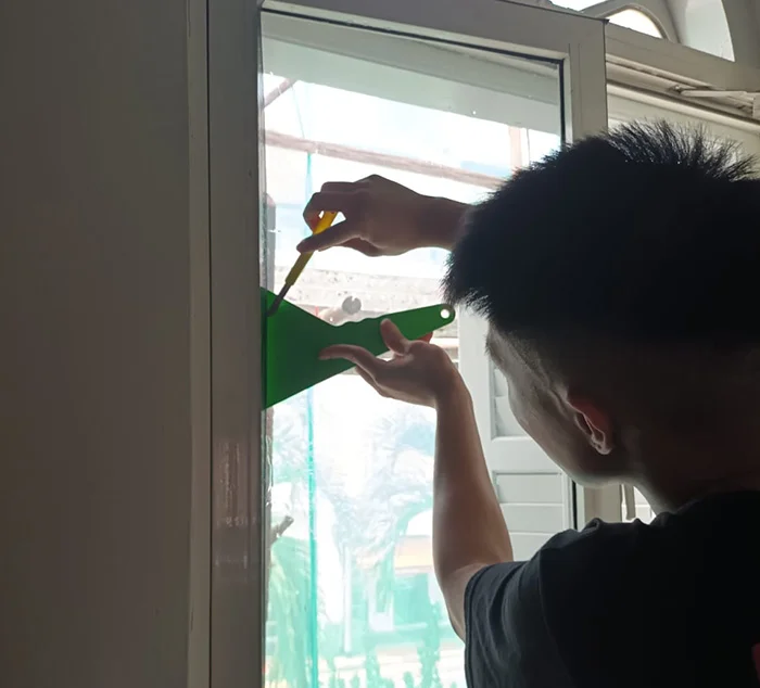 Technician installing solar film on HDB window using squeegee to reduce heat and glare in a Singapore home